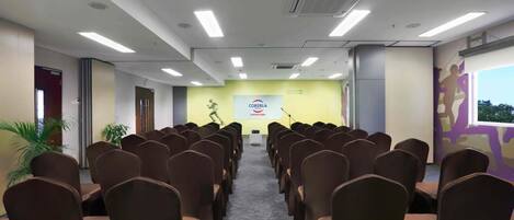 A conference room with rows of chairs facing a podium, a large banner on the wall, and a window with a view of trees.