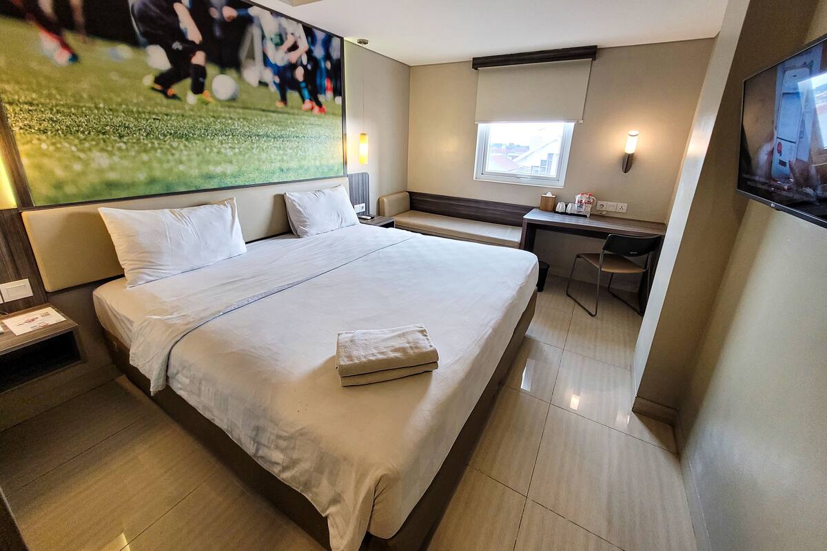 Une chambre d’hôtel avec un grand lit, un bureau, une chaise, une fenêtre et un téléviseur fixé au mur.