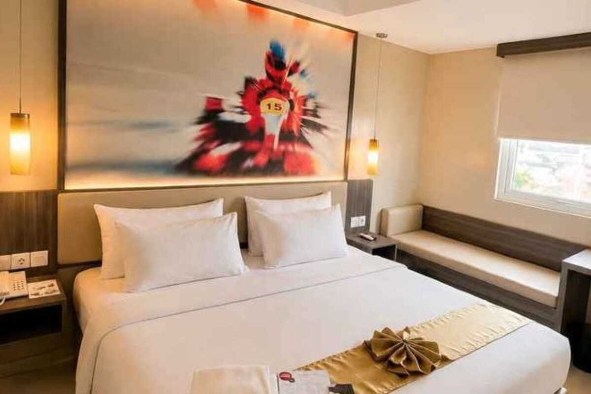 Habitación de hotel con una cama grande, mesitas de noche, un banco y un cuadro en la pared.