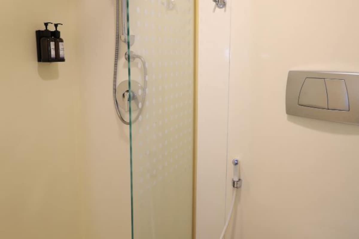 Un baño con cabina de ducha de vidrio, dispensador de jabón e interruptor de luz.