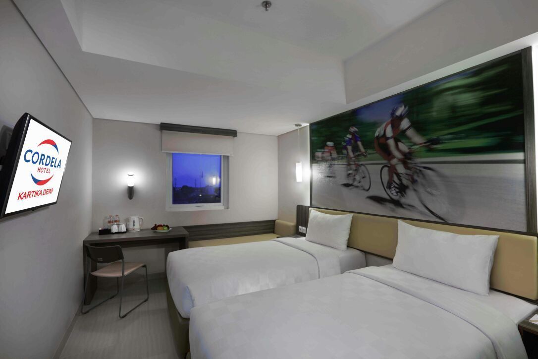 Habitación de hotel con dos camas, un escritorio, una silla, un televisor y un cuadro de ciclistas.