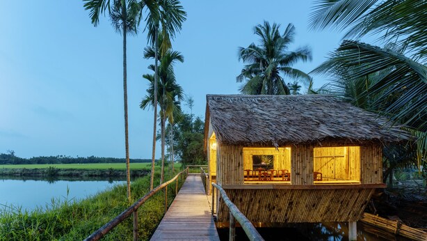 A wooden structure with a thatched roof over water, connected by a wooden walkway. - New Sunshine Homestay (Da Nang)