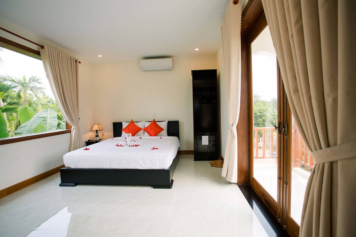 A bedroom with a bed, a nightstand, a TV, and a balcony with curtains.