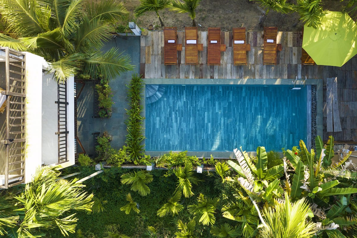 A rectangular swimming pool surrounded by wooden deck chairs and a wooden fence.
