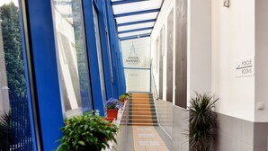Un pasillo con plantas en macetas, una escalera y un cartel que dice 'POKOJE ROOMS'.