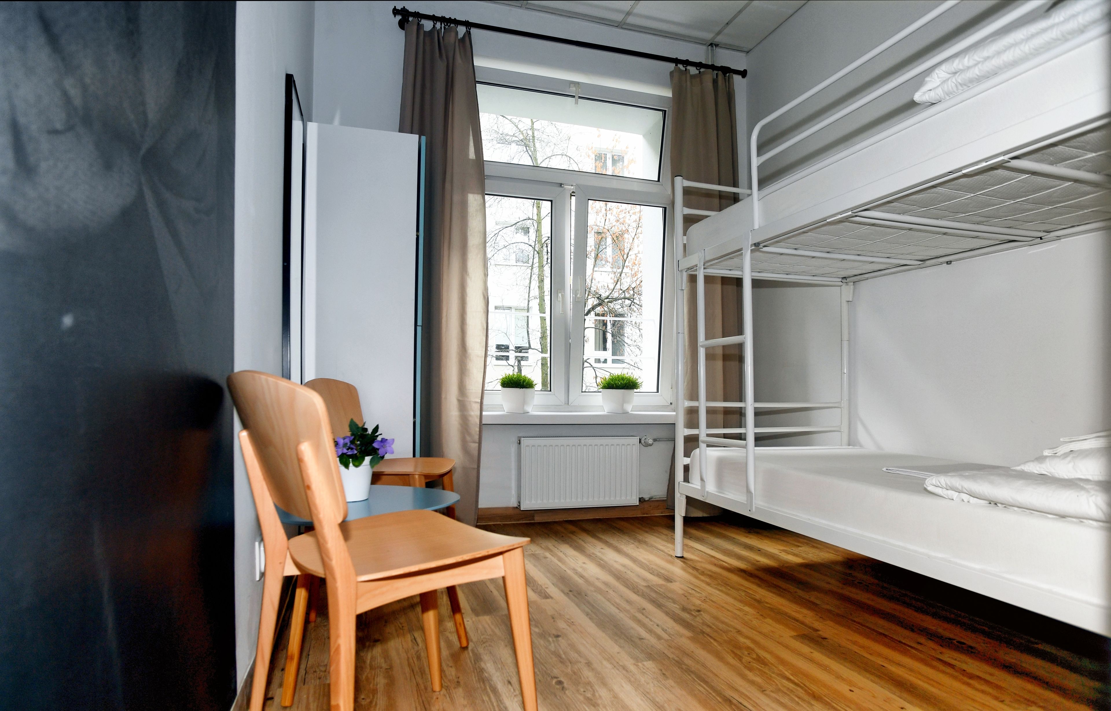 A room with a bunk bed, a wooden table with chairs, a window with curtains, and a radiator.
