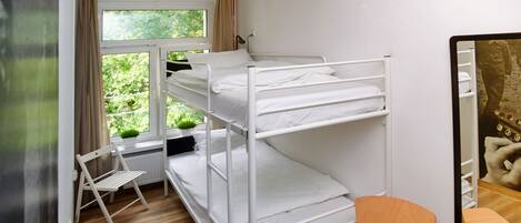 A bunk bed room with a desk, chair, and a window with curtains.