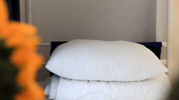 A bed with white bedding and a dark headboard in a room with white walls.