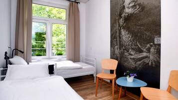 A hotel room with two beds, a small table with a chair, a window with curtains, and a large abstract painting on the wall.