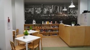 Una biblioteca con un mural de paisaje urbano, mesas y sillas de madera y estanterías.