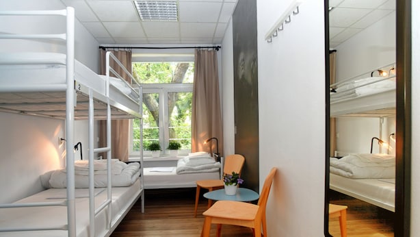 Un dormitorio con literas, una pequeña mesa con sillas, una ventana con cortinas y un espejo en la pared.