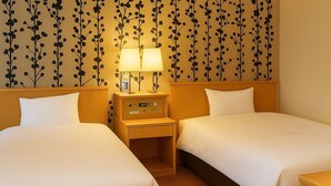 Une chambre d’hôtel avec deux lits, une table de chevet avec une lampe et un mur orné d’un motif floral.