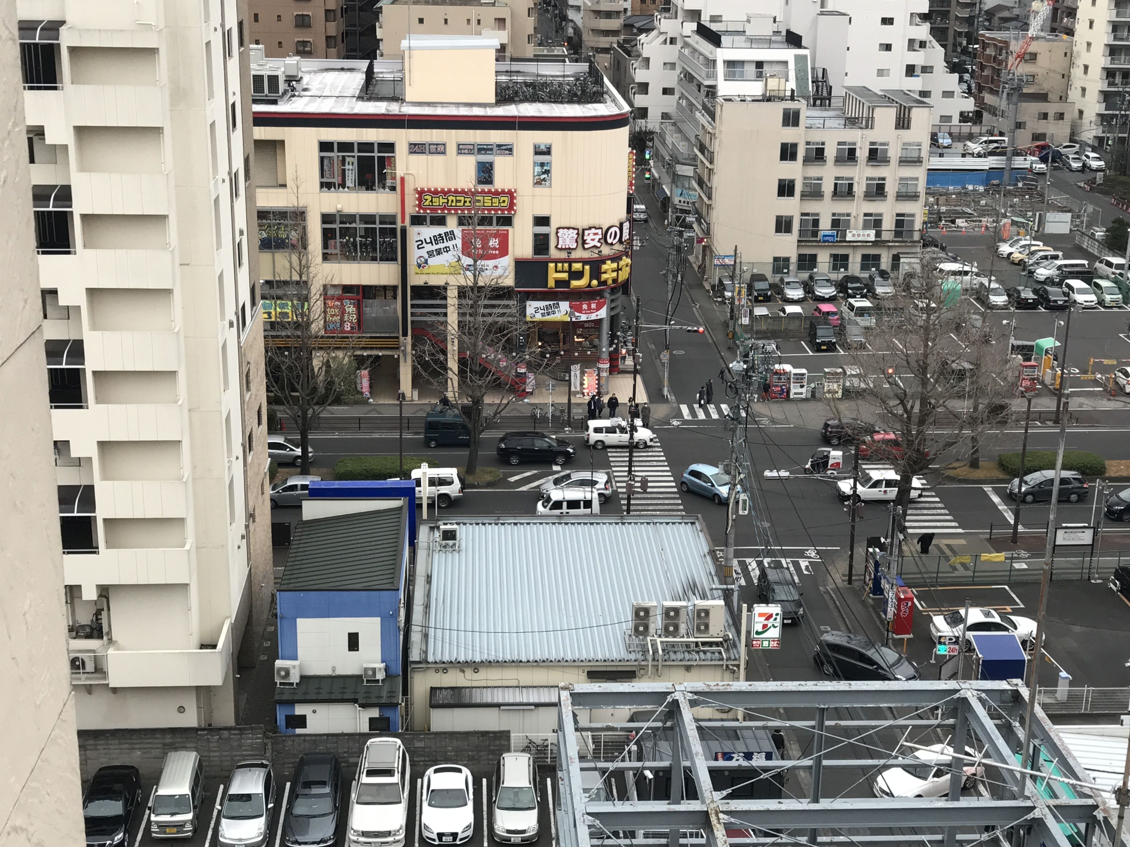A multi-story building with a commercial ground floor, parking spaces, and a pedestrian crossing.