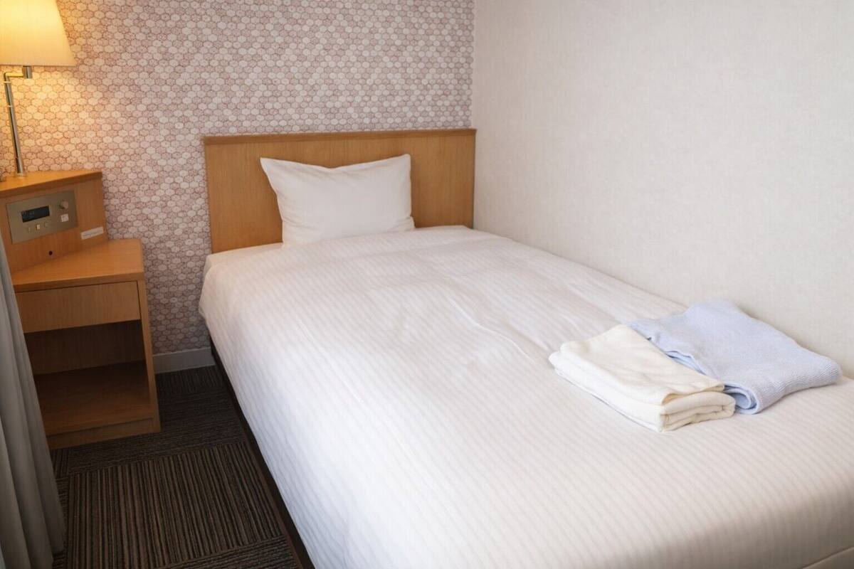 A single bed with a wooden headboard, a bedside table with a lamp, and a patterned wall.