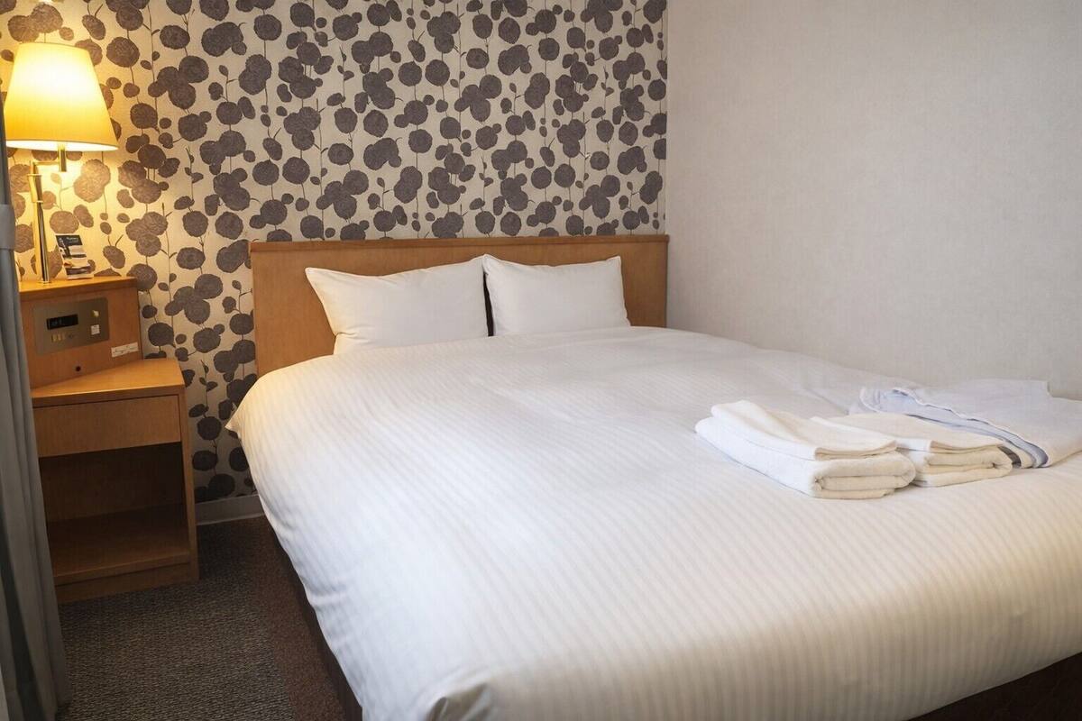 A neatly made bed with white linens, a wooden headboard, and a nightstand with a lamp and a clock.