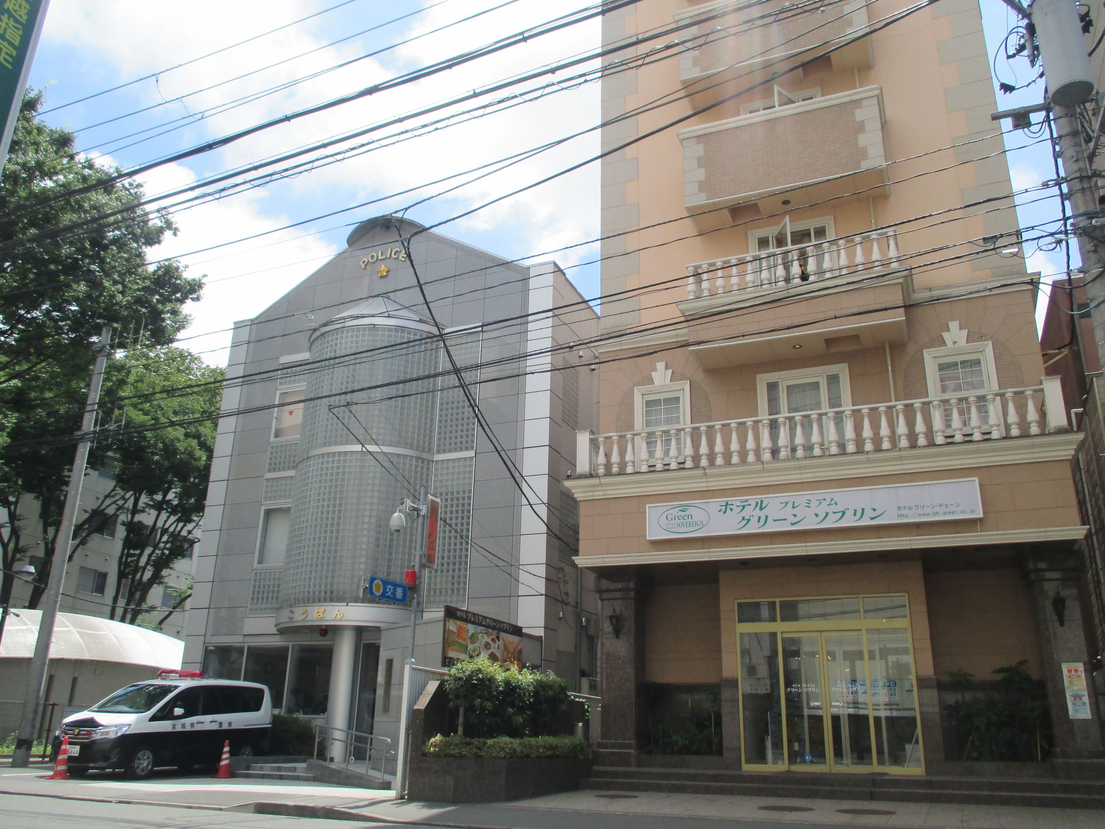 Un bâtiment sur lequel on peut voir une enseigne indiquant qu’il s’agit d’un poste de police, une enseigne verte avec du texte en japonais, et une entrée fermée par un portail.