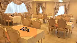 Une salle de banquet dotée de nombreuses tables rondes, de chaises richement décorées et de lustres.