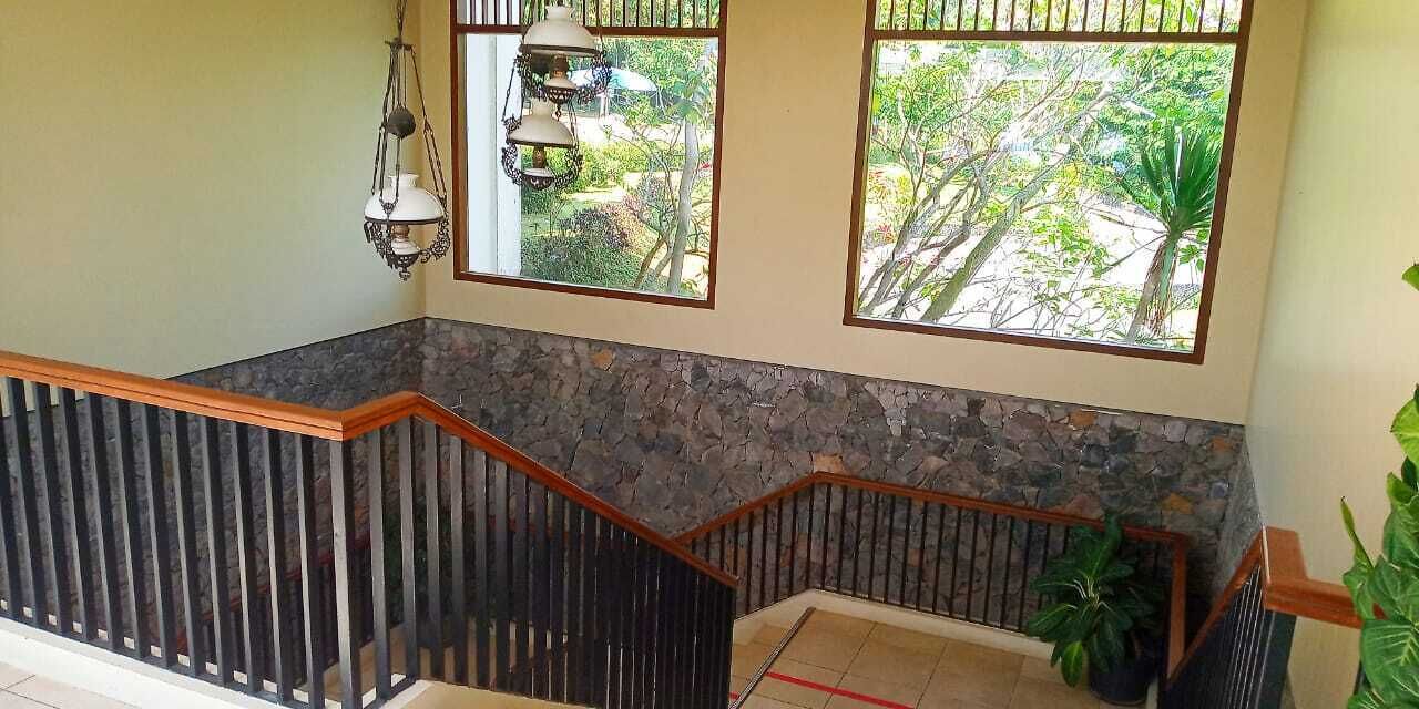 Un escalier avec un mur en pierre et une rampe en bois, menant à un balcon d’où l’on peut admirer la verdure.