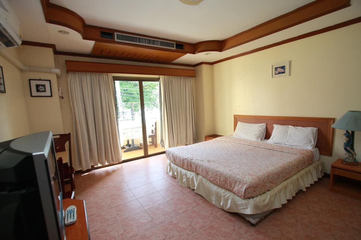 A hotel room with a large bed, a television, and a sliding glass door to the outside.