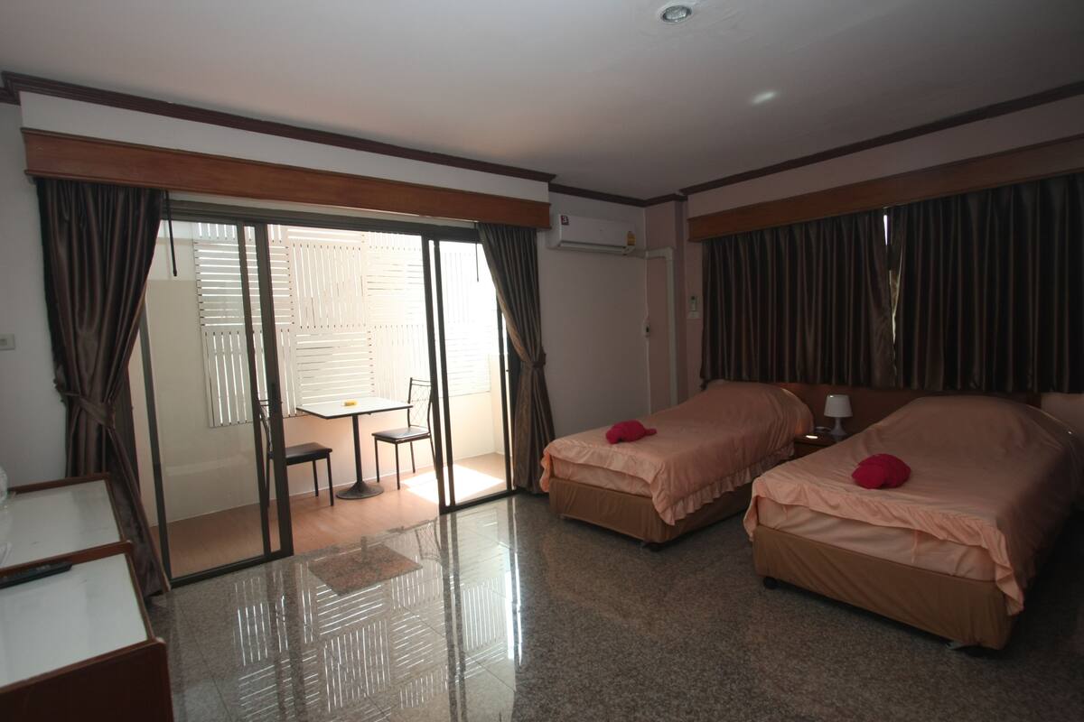 A hotel room with two beds, a desk, and a chair. There is a sliding glass door leading to a balcony.