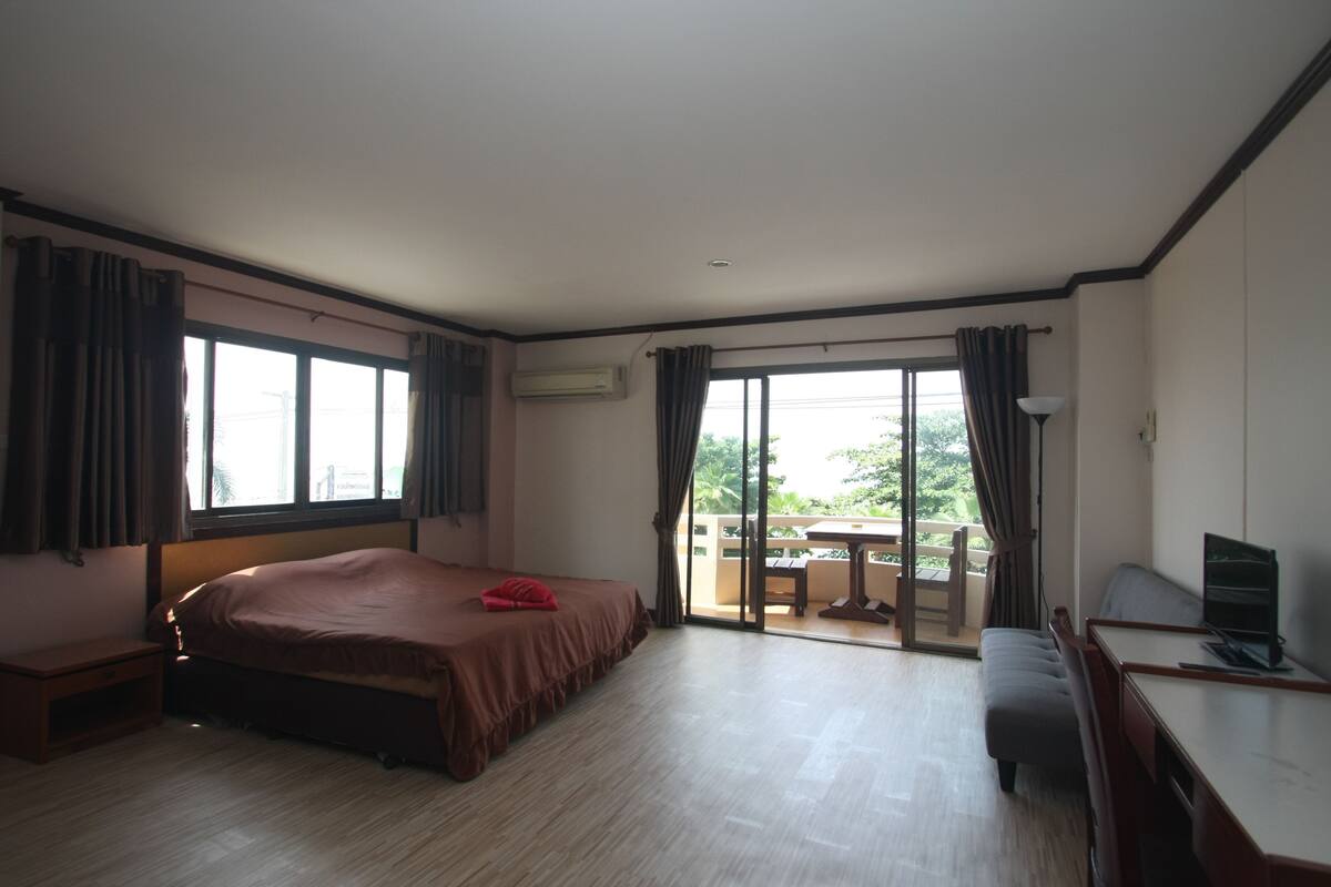 A hotel room with a bed, a desk, a chair, and a balcony with a table and chairs.