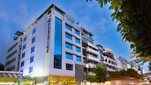 A multi-story hotel with a prominent sign, large windows, and a street view with moving vehicles. - The Prestige Nana (Bangkok)