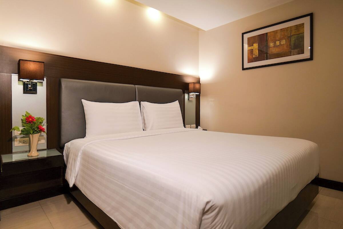 A neatly made bed with a headboard, a bedside table with a vase of flowers, and a framed picture on the wall.