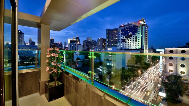 A balcony with a view of a cityscape at dusk, featuring modern buildings and a busy street below. - The Prestige Nana (Bangkok)