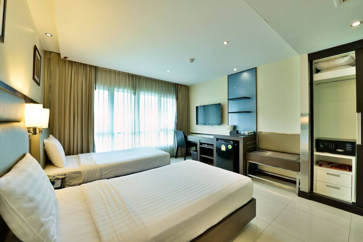 A hotel room with two beds, a desk, a TV, and a minibar.