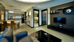 A modern living room with a sofa, coffee table, and TV. There is a kitchen in the background with a dining area. - The Prestige Nana (Bangkok)
