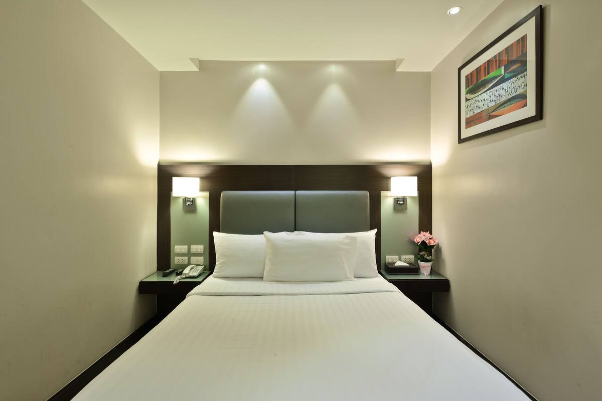 A hotel room with a large bed, two bedside tables, a nightstand, a lamp, and a framed picture on the wall.