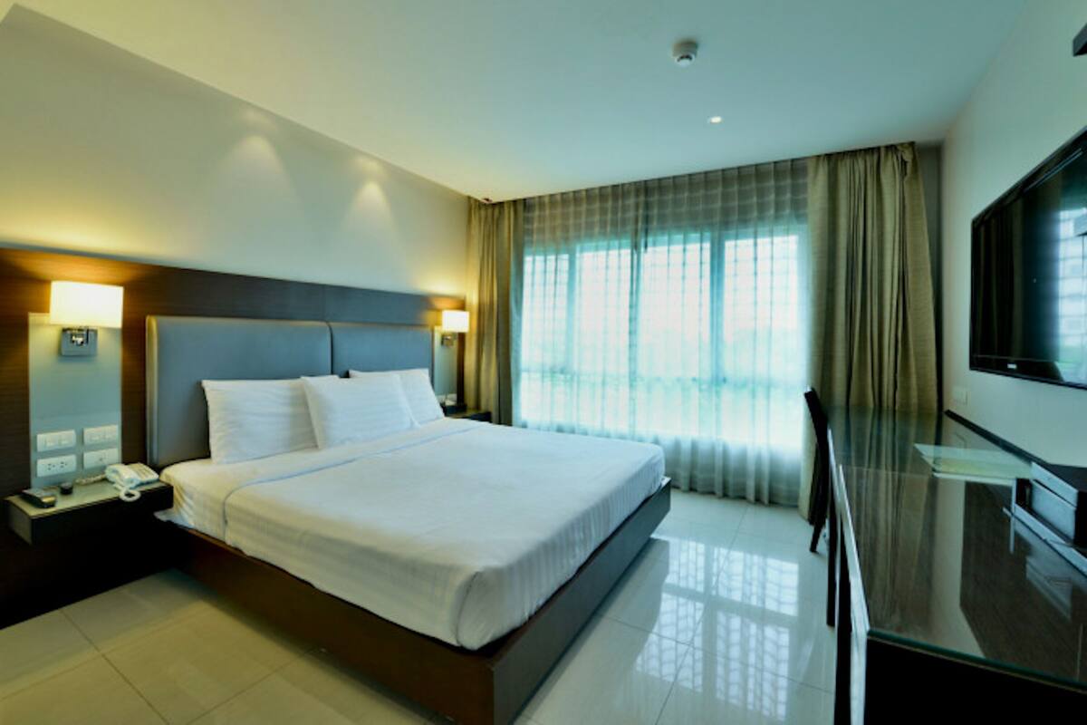 A hotel room with a large bed, bedside lamps, a flat-screen TV, and a glass coffee table.