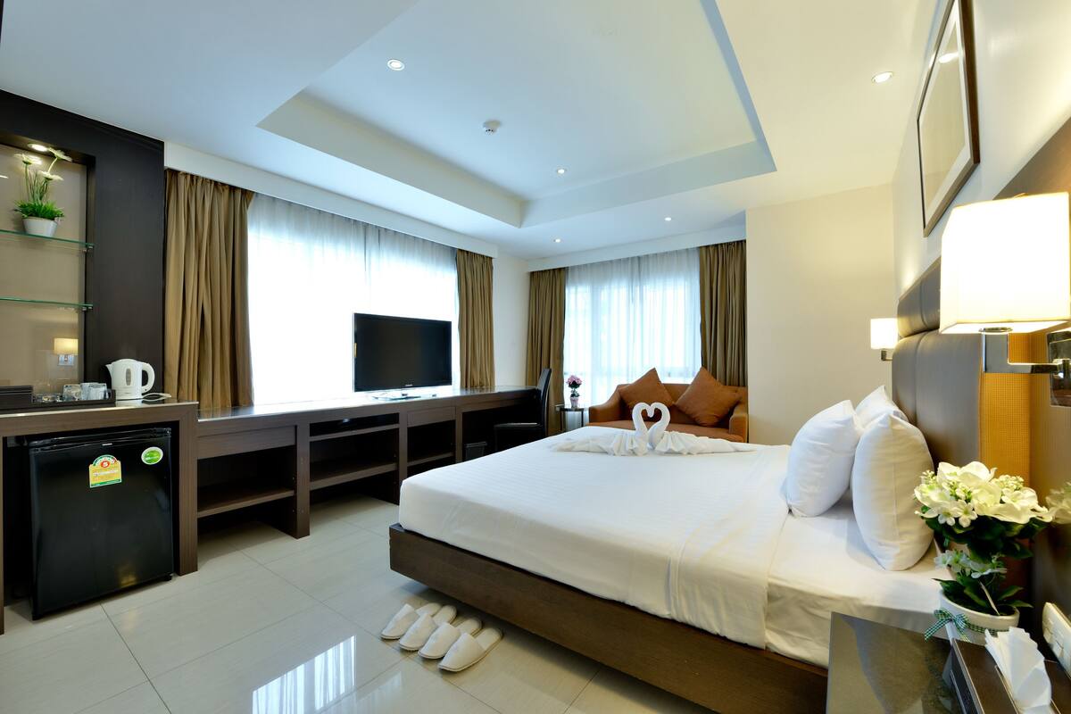 A hotel room with a large bed, a desk with a television, a small refrigerator, and a window with curtains.