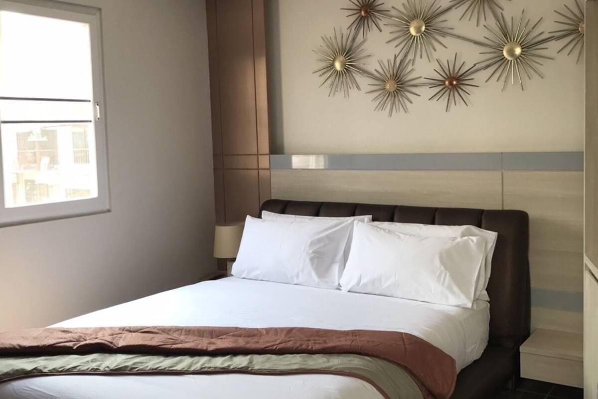 Uma cama bem arrumada com lençóis brancos, cabeceira marrom e um objeto decorativo acima.