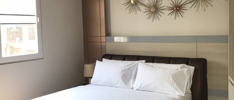 A neatly made bed with white linens, a brown headboard, and a decorative wall piece above it.