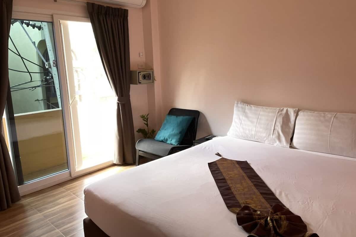 Quarto de hotel com cama, uma cadeira, janela com cortinas e ar condicionado.