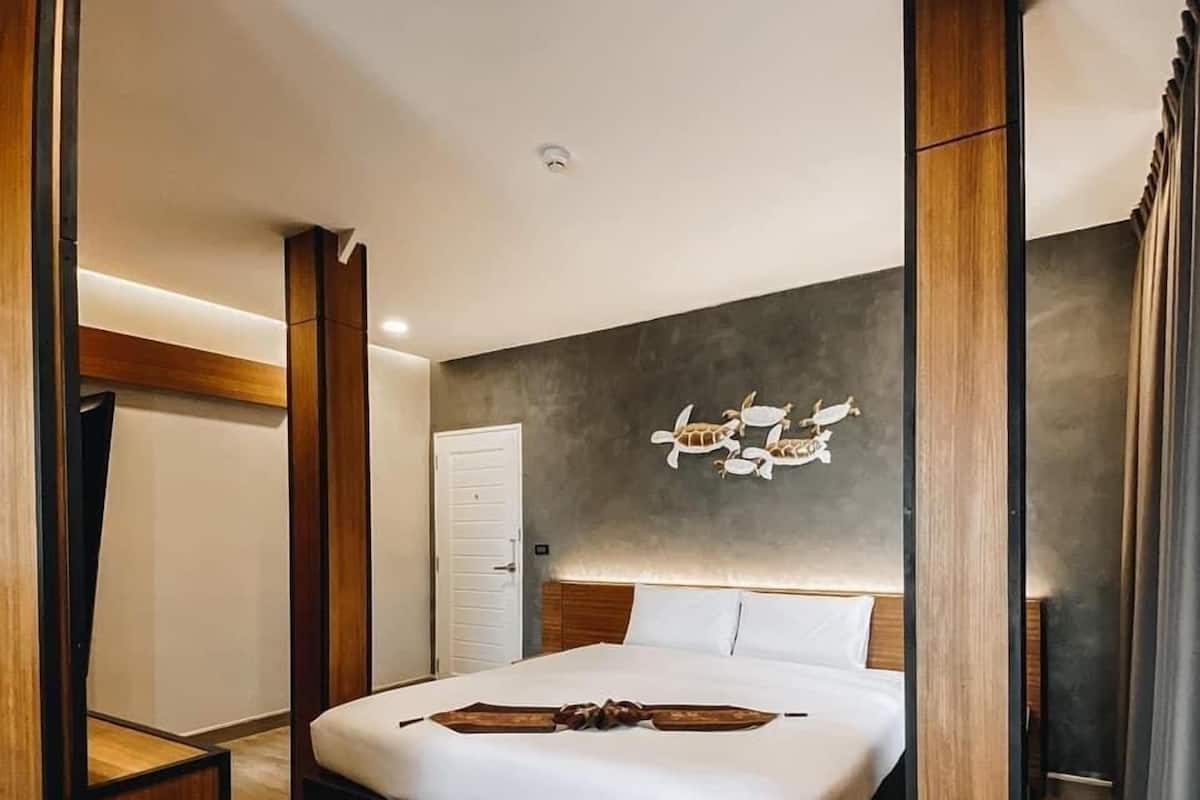 Quarto moderno com uma cama grande, piso de madeira, porta branca e parede com mural de tartaruga.