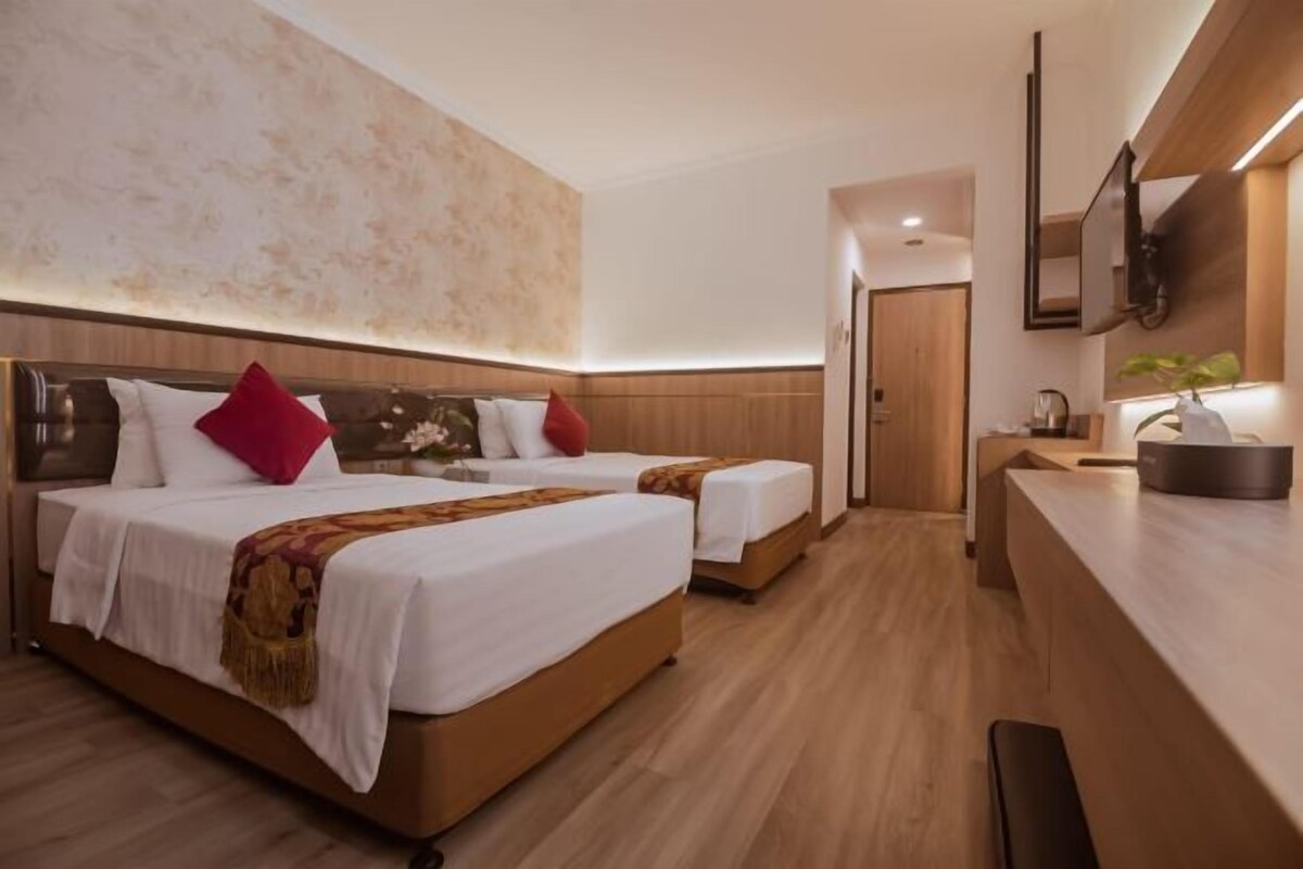 Hotellihuone, jossa on kaksi sänkyä, puinen pääty, yöpöytä, peili ja pieni keittokomero.