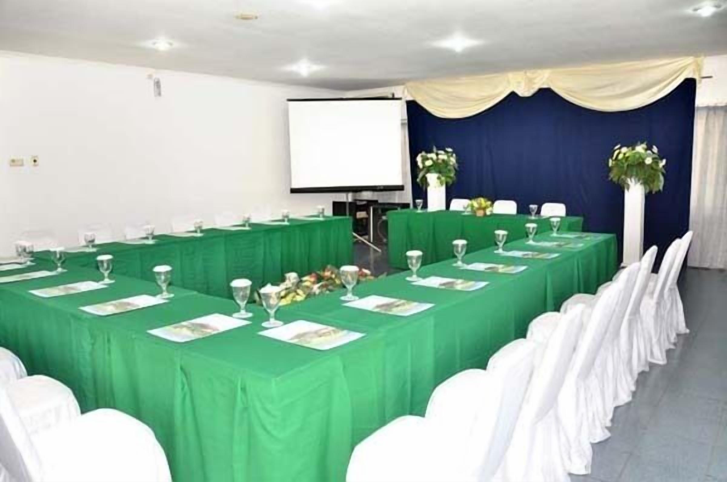 A conference room with a long table set for a meeting, white chairs, and a projector screen.