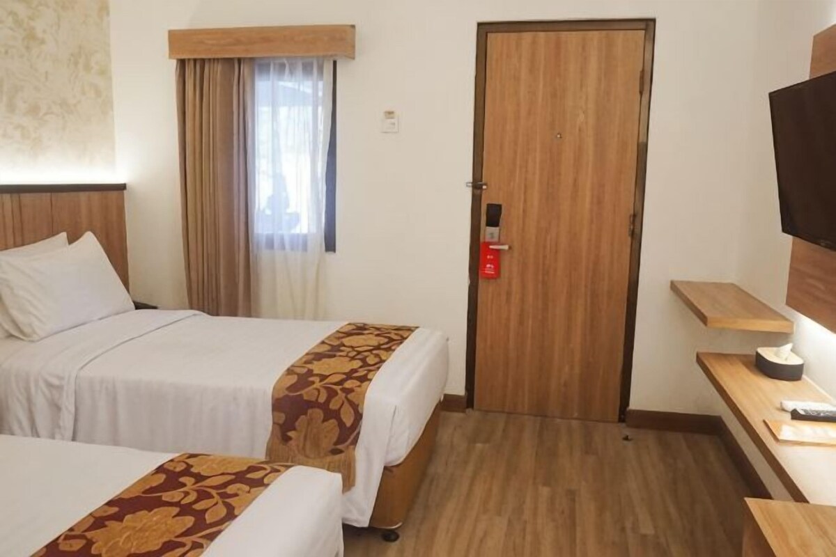 Hotellihuone, jossa on kaksi sänkyä, puuovi, televisio ja pieni pöytä.