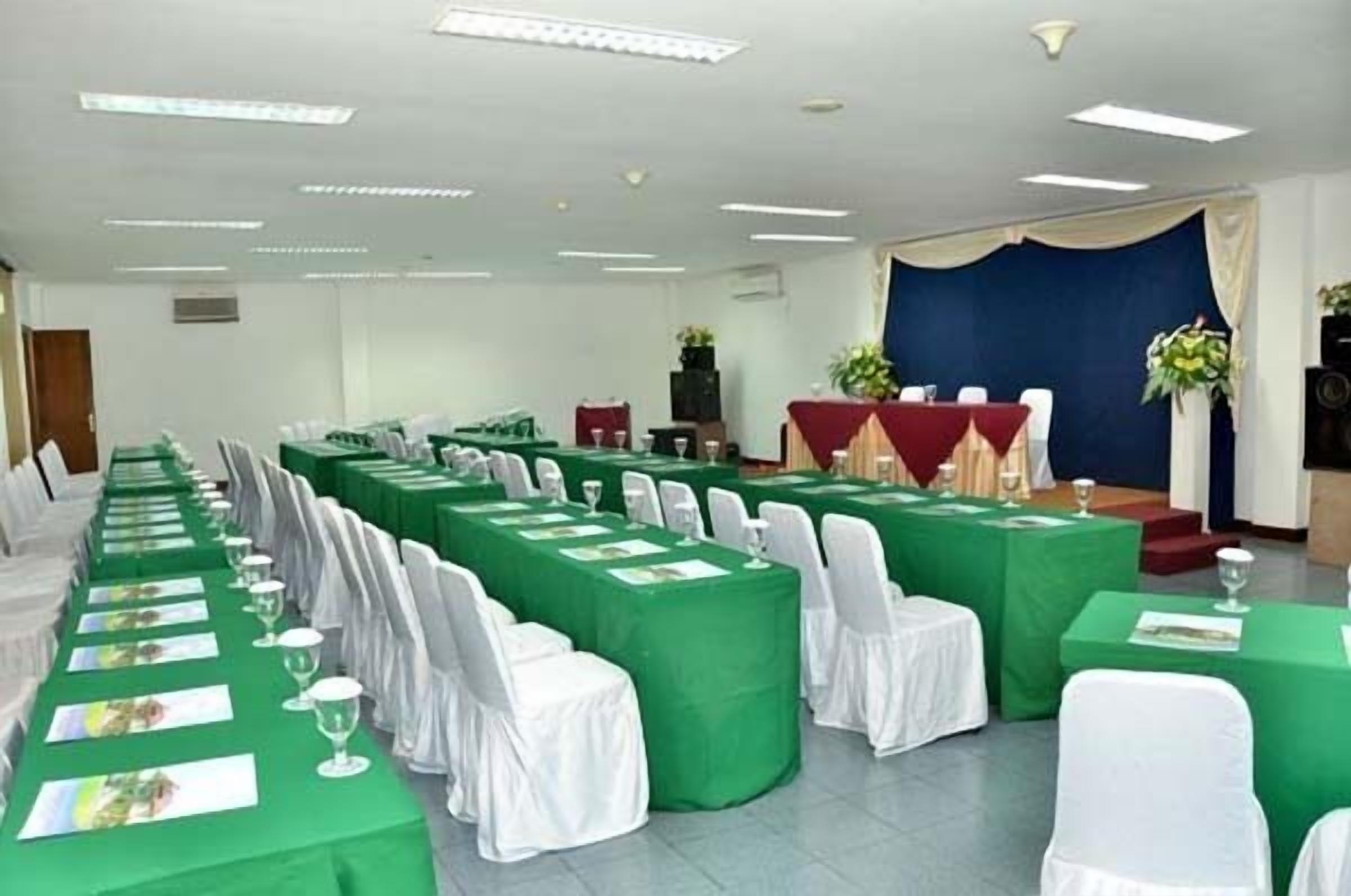 A conference room with rows of tables covered in green tablecloths, white chairs, and name cards.