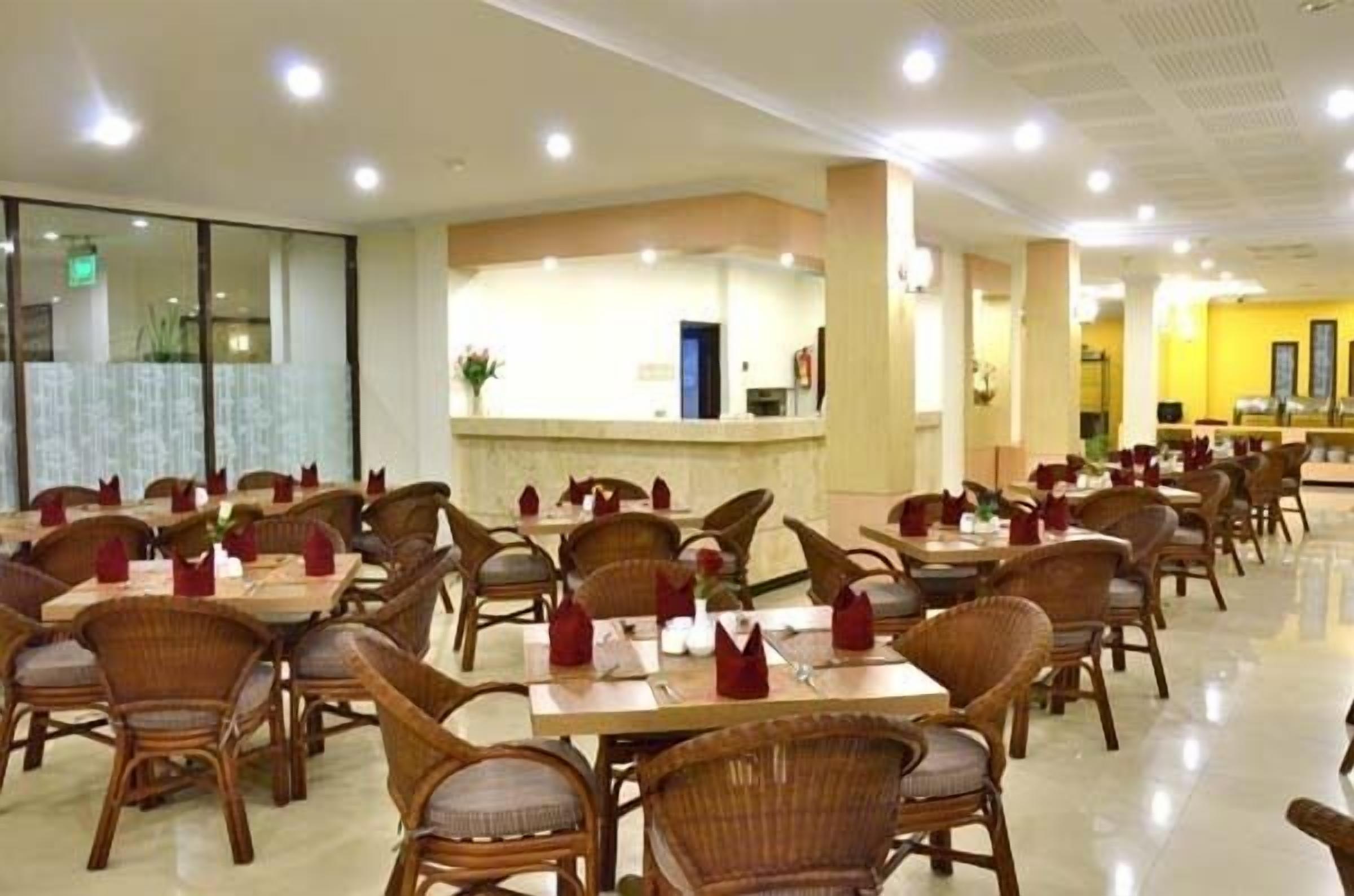 A spacious dining area with wicker chairs and tables, a reception desk, and a yellow accent wall.