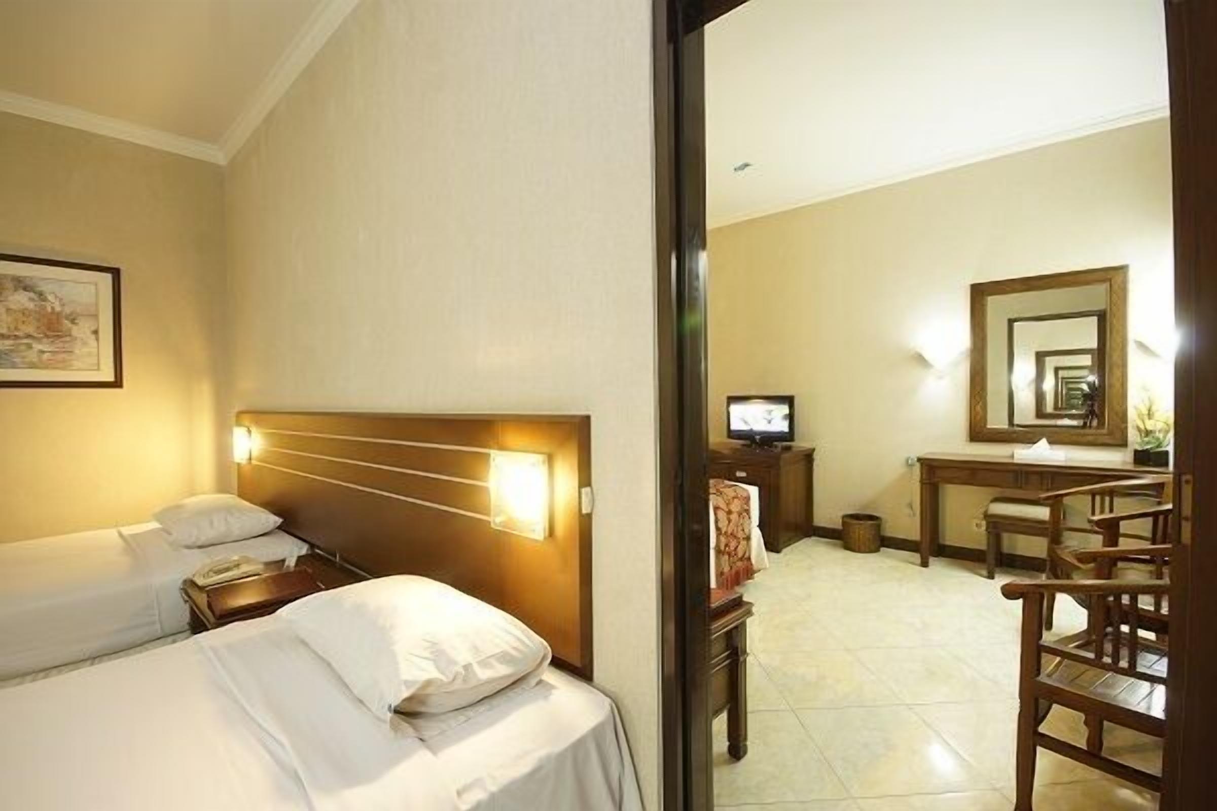 Una habitación de hotel con dos camas, un escritorio, una silla, un televisor y un espejo.