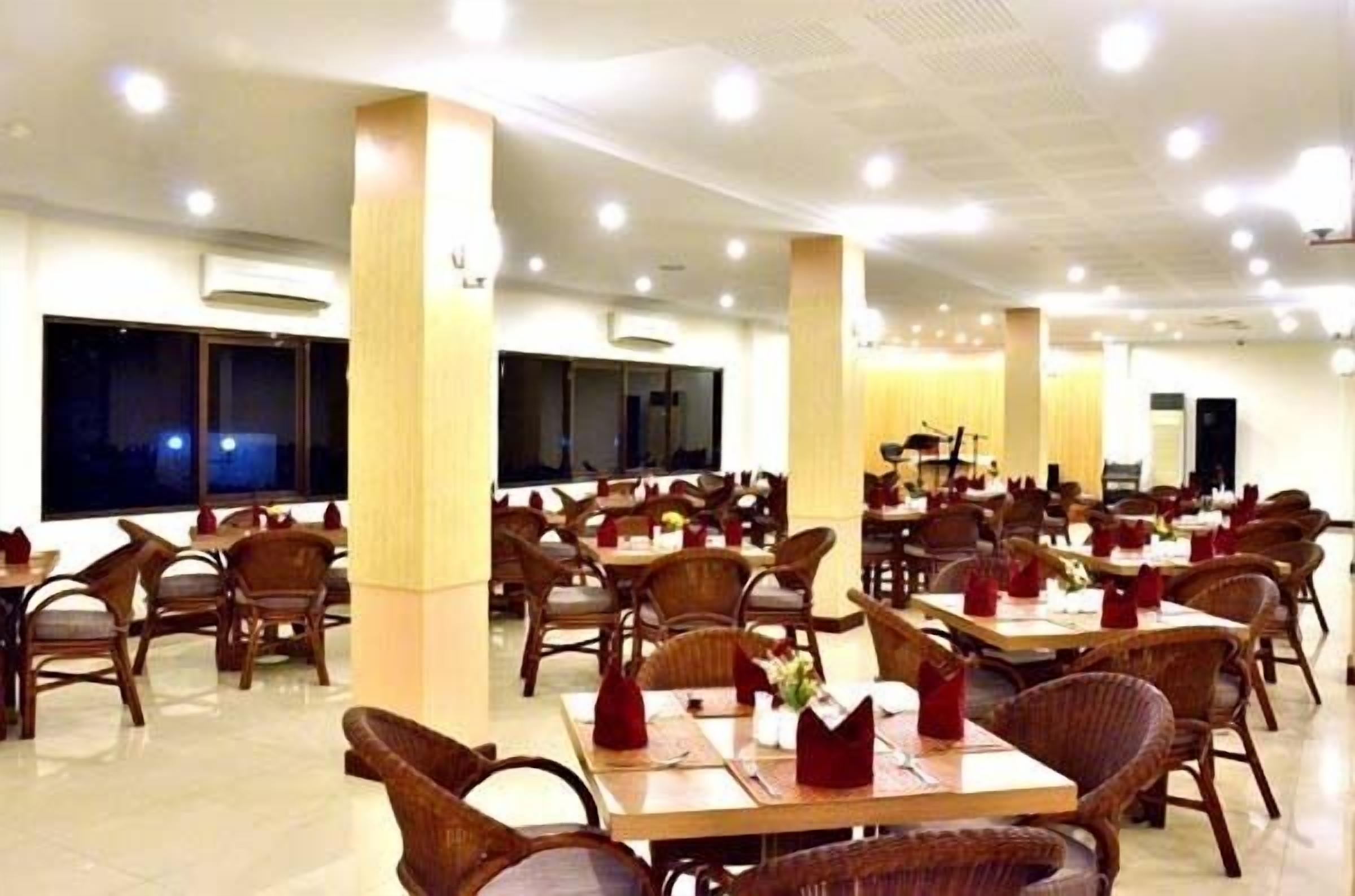 A spacious dining area with multiple tables and chairs, large windows, and ceiling lights.