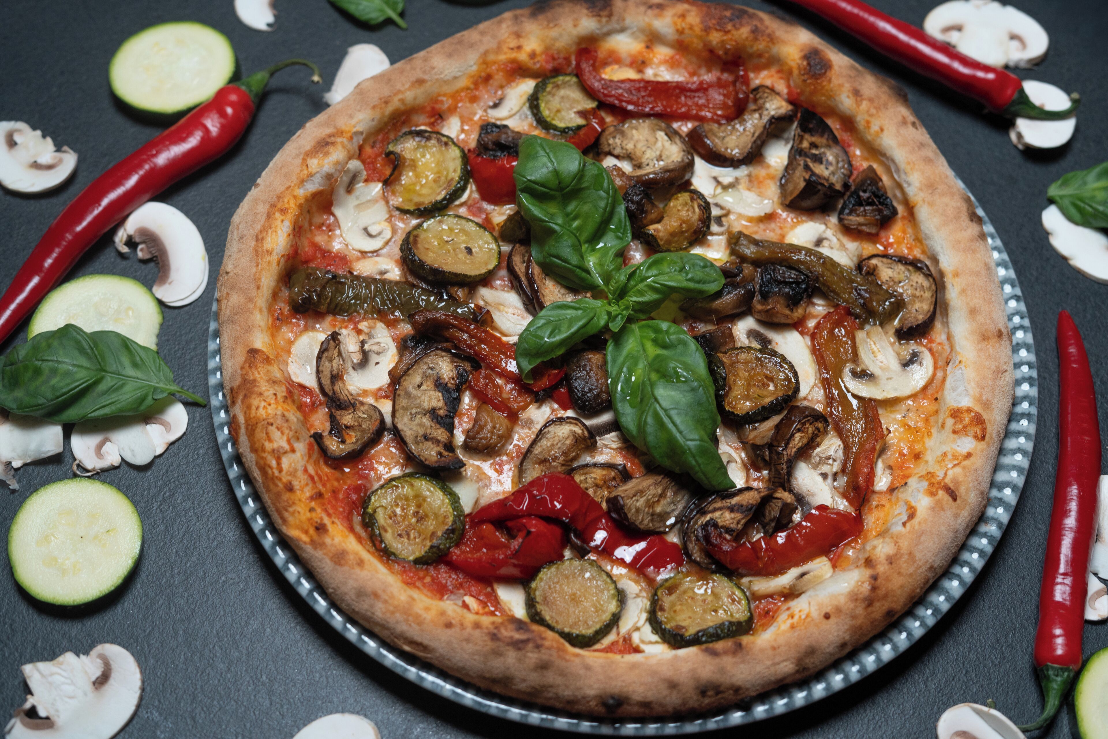 A pizza with various toppings and vegetables on a metal tray.