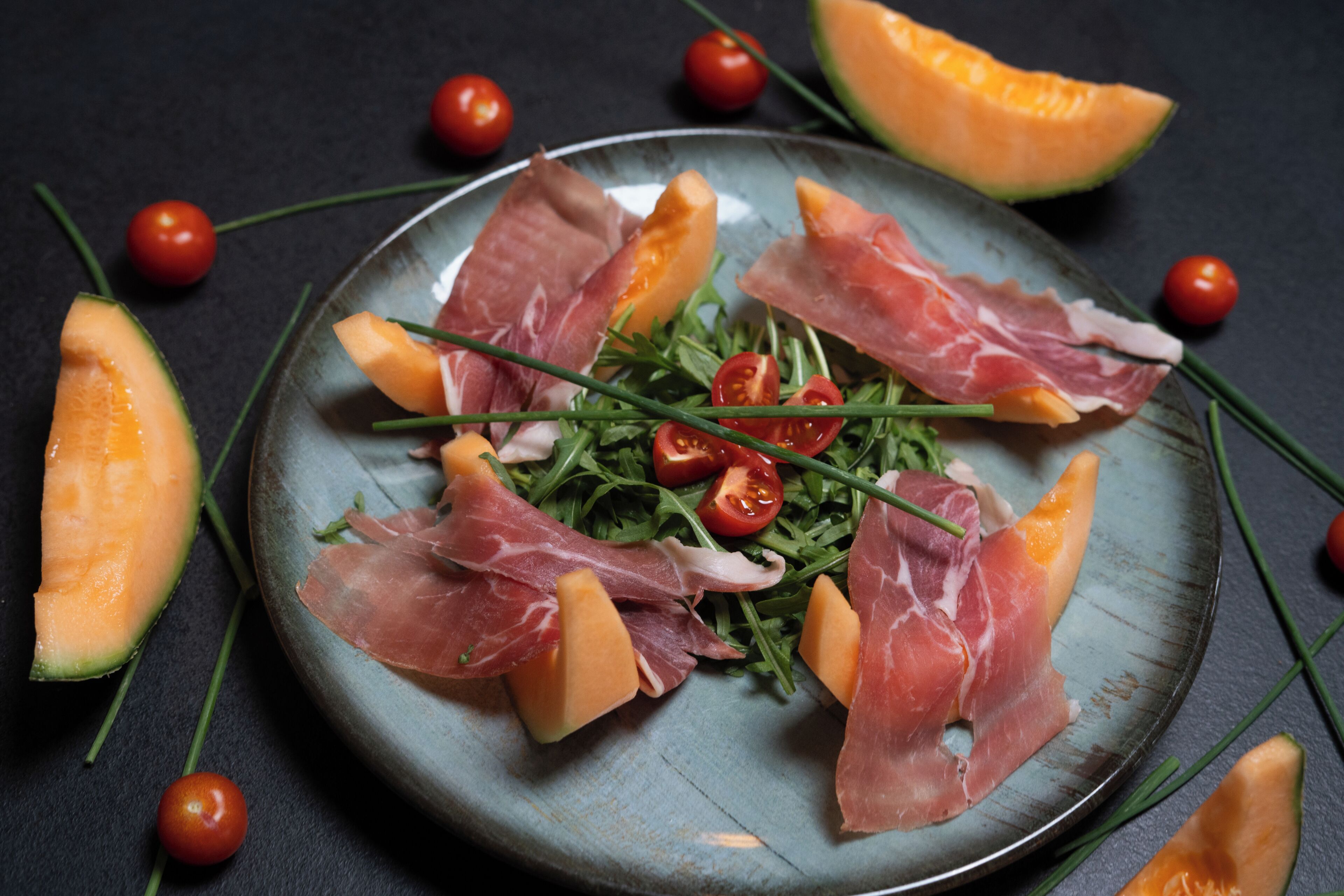 Un plato con jamón serrano, rúcula, tomates cherry y melón en rodajas.