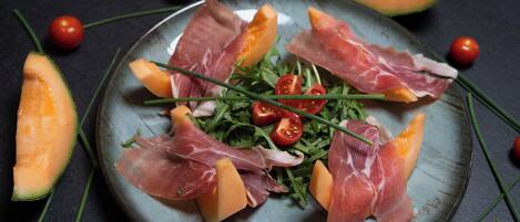 Un plato con jamón serrano, rúcula, tomates cherry y melón en rodajas.