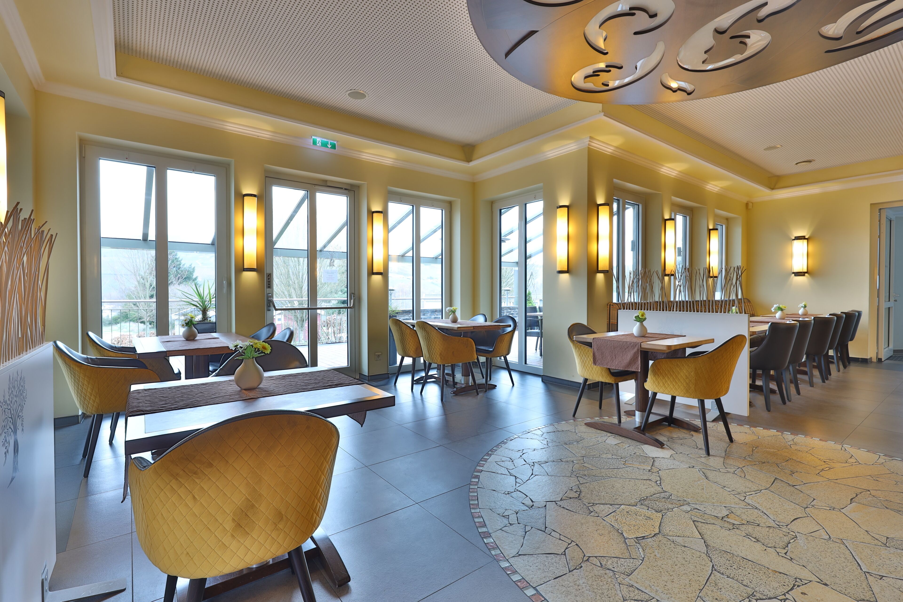 A spacious dining area with multiple tables and chairs, large windows, and a patterned floor.