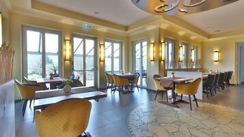 A spacious dining area with multiple tables and chairs, large windows, and a patterned floor.