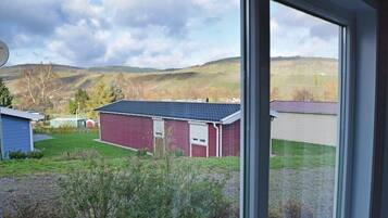 A view of a red building with a dark roof, surrounded by a grassy area and a hill in the background.